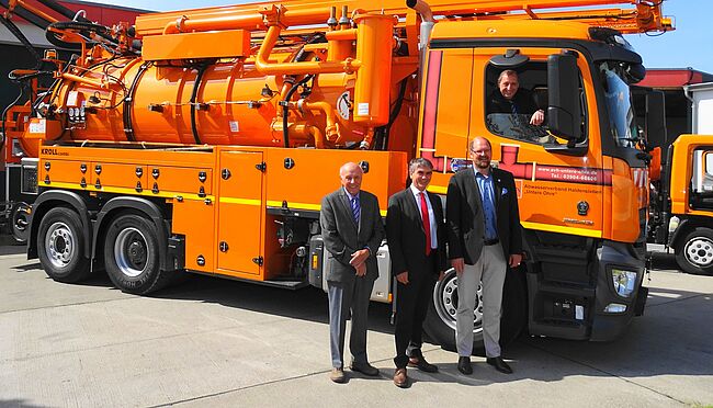 Foto Abwasserzweckverband "Untere Ohre" Haldensleben / Landrat Martin Stichnoth und Staatsekretär Steffen Eichner gratulieren Achim Grossmann (Fenster) und Verbandsverteter Wilhelm Behrens zum Jubiläum. Achim Grossmanns schaut aus dem Fenster eines Abwasserfahrzeuges. Die anderen Herren stehen davor.