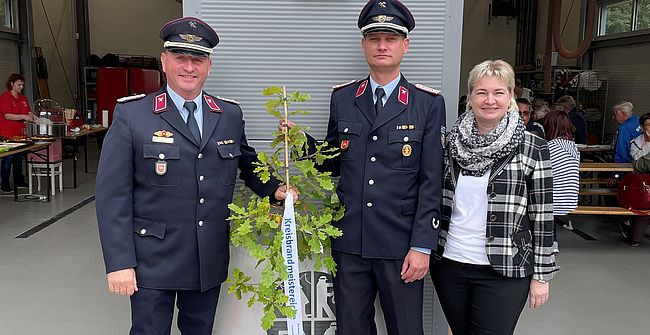 Vor den beiden Toreinfahren des Feuerwehrgerätehauses in Rottmersleben haben Kreisbrandmeister Matthias Schumann, Ortswehrleiter Thomas Brzezinski und Amtleiterin Corinna Sladky Aufstellung zum Erinnerungsfoto genommen. Der Kreisbrandmeister überreicht einen "Eichensetzling".
