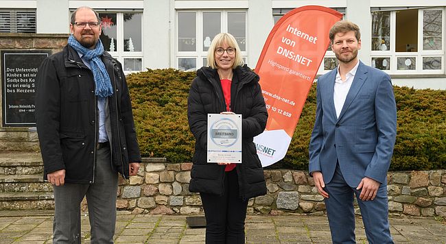 DAs Foto zeigt 3 Personen vor der Förderschule in Klein Oschersleben, von links nach rechts Landrat martin Stichnoth, Schulleiterin Silke Heick mit dem Zertifikat in den Händen und Widar Wendt (atene-kom).