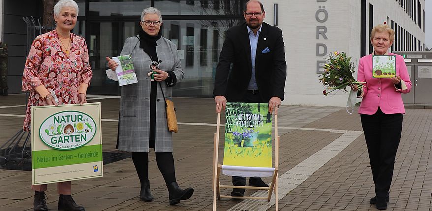 Die Akteure stehen mit Werbematerialien vor dem Verwaltungsgebäude des Landkreises Börde in Haldensleben. Daniela Süssmann, Christa Ringkamp und Steffi Trittel informieren Landrat Martin Stichnoth über den aktuellen Stand der Planungen. Stichnoth, Schirmherr der Ausstellung steht hinter einem Liegestuhl mit dem Werbeaufdruck "Gartensommer".