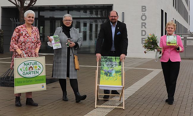Die Akteure stehen mit Werbematerialien vor dem Verwaltungsgebäude des Landkreises Börde in Haldensleben. Daniela Süssmann, Christa Ringkamp und Steffi Trittel informieren Landrat Martin Stichnoth über den aktuellen Stand der Planungen. Stichnoth, Schirmherr der Ausstellung steht hinter einem Liegestuhl mit dem Werbeaufdruck "Gartensommer".