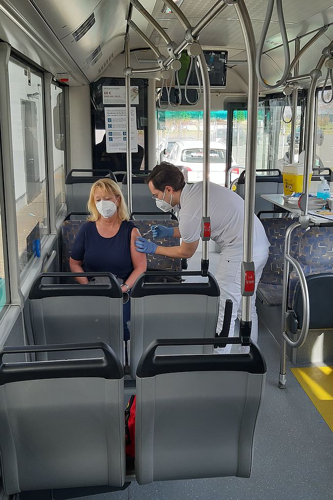 Das Foto zeigt einen Einblick in das "Innere" eines Impfbusses. Ein impfberechitgte Person nimmt im Bild die Impfung vor 