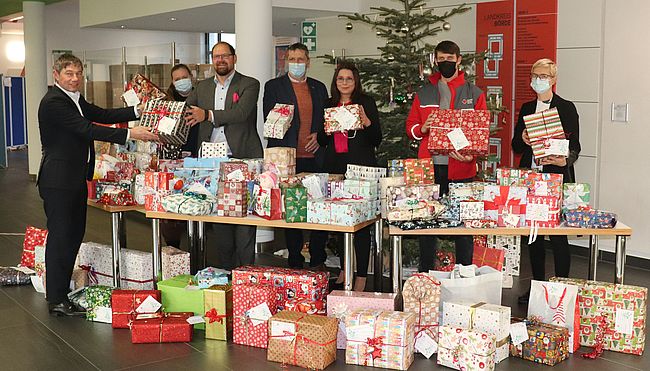 Das Foto zeigt eine Weihnachtsbaum und davor zahlreiche Geschenke. Landrat Martin Stichnoth übergibt die Geschenke vom Weihnachtswuschbaum in Haldensleben an DRK-Vorstand Ralf Kürbis. Im Bild weitere Mitarbeiter des Landkreises und des DRK Kreiserbandes Börde.