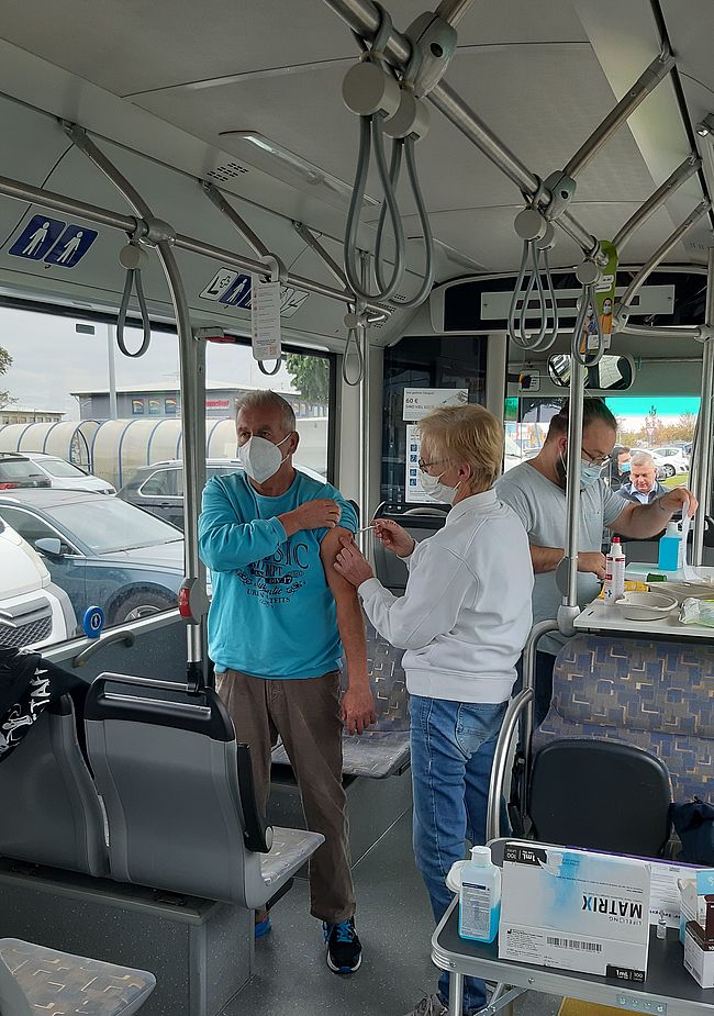 Das Foto zeigt das Innere eines Impfbusses. Ein impfberechtigte Person setzt Otto Schönfeld aus Kunrau eine Schutzimpfung. Eine weitere Person zieht im Hintergrund eine neue Spritze auf.