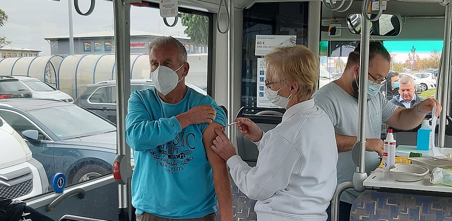 Das Foto zeigt das Innere eines Impfbusses. Ein impfberechtigte Person setzt Otto Schönfeld aus Kunrau eine Schutzimpfung. Eine weitere Person zieht im Hintergrund eine neue Spritze auf.