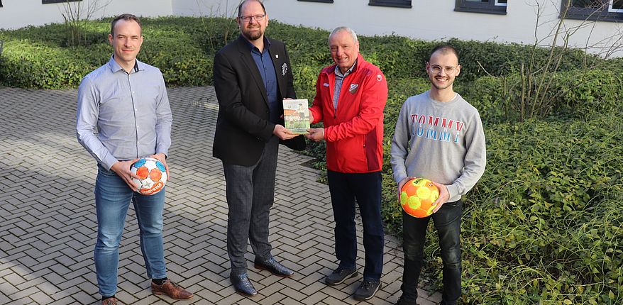 Das Foto zeigt Dietrich Lehmann bei der Übergabe des Buches an Martin Stichnoth, daneben zwei sportbegeisterte Mitarbeiter der Kreisverwaltung, links Domenik Siegmund, selbst aktiv beim Eilslebener Sportverein, und Kilian Paetzel, Nachwuchstrainer „NFZ“ Oschersleben, ausgestattet mit der C-Trainer-Lizenz.