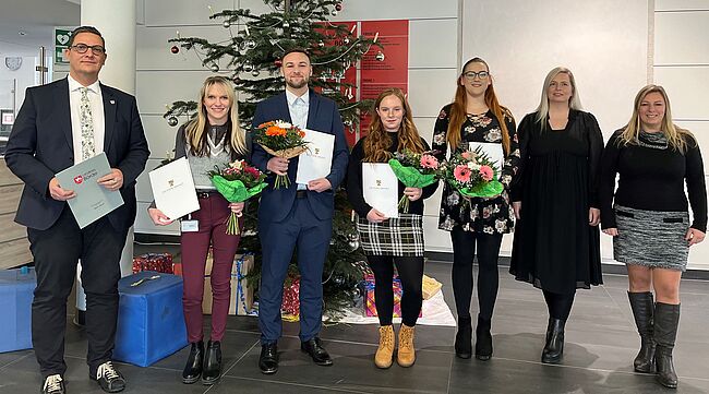 Foto Uwe Baumgart / Aufstellung zum Erinnerungsfoto (v.l.n.r.) Beigeordneter Dr. Marcus Waselewski, Laura Patermann, Leon Gäde, Hannah Pientka, Kimberly Könnecke, Personalchefin Julia Herzberg-Ebeling und Ausbildungsleiterin Manuela Brasch. Hintergrund, ein Weihnachtsbaum.