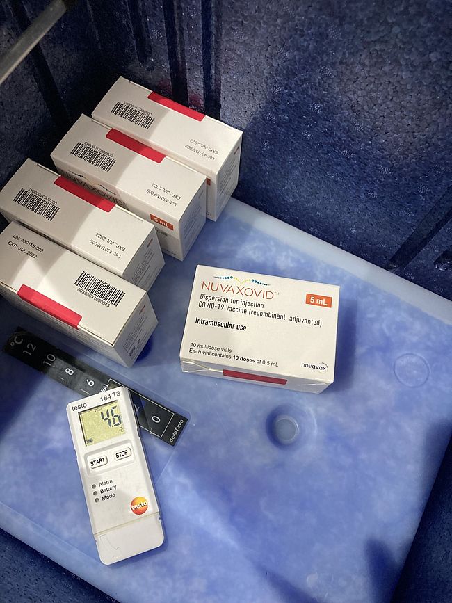 Das Foto zeigt ein Motiv auf die Schachteln, in denen der Impfstoff Nuvaxodid von Novavax verpackt ist. Die Packungen liegen in einer Box, die Temperatur wir duch ein inneliegendes Thermometer überwacht. 