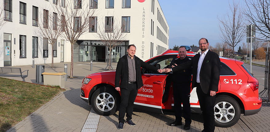 Uwe Baumgart / Rafael von Malottki übergibt die gesponserten "BOS-Handfunksprechgeräte" im Beisein von Landrat Martin Stichnoth an Matthias Schumann (Vorsitzender Förderverein Feuerwehr Zielitz und Kreisbrandmeister Landkreis Börde). Das Foto, im Hintergrund das Einsatzfahrzeug des Kreisbrandmeisters und das Verwaltungsgebäude des Landkreises Börde.