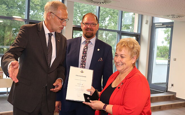 das Foto zeigt Heinz-Lothar Theel und Landrat Martin Stichnoth bei der Auszeichnung. Im Vordergrund Iris Herzig. Sie erhält die Ehrennadel und die dazugehörige Urkunde. Alle Akteure im Bild freuen sich.