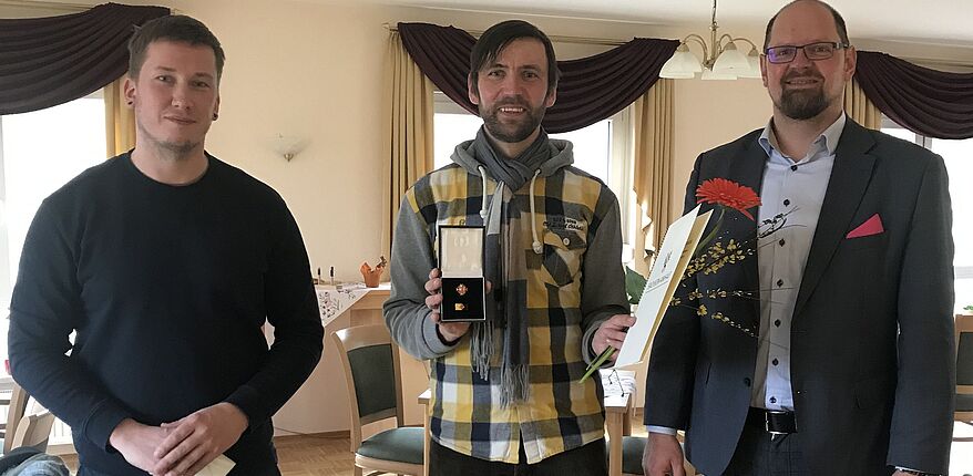 Foto Juliane Herm / Landrat Martin Stichnoth und der Landtagsabgeordnete Tim Teßmann zeichnen Ruben Herm mit der Ehrennadel des Landes Sachsen-Anhalt aus. Herm steht zwischen den beiden Herren. Er hat die Nadel und die Urkunde in den Händen. 
