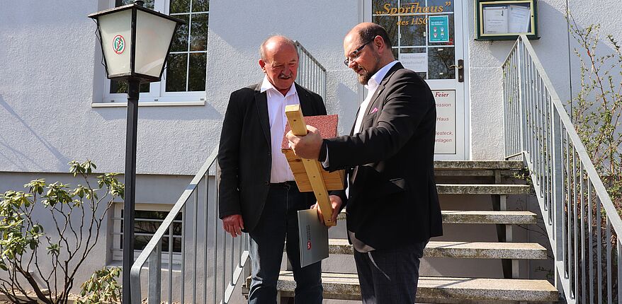 Foto Landkreis Börde / Landrat Martin Stichnoth verabschiedet vor dem Vereinsheim des Haldensleber Sportclubs Kreissportbundgeschäftsführer Hartmut Baethge in den Ruhestand. Die beiden Herren stehen vor dem Eingang in die Clubgaststätte. 