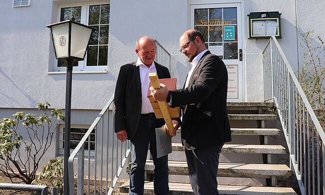 Foto Landkreis Börde / Landrat Martin Stichnoth verabschiedet vor dem Vereinsheim des Haldensleber Sportclubs Kreissportbundgeschäftsführer Hartmut Baethge in den Ruhestand. Die beiden Herren stehen vor dem Eingang in die Clubgaststätte. 