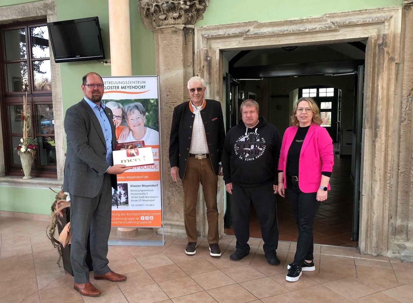 Foto Landkreis Börde / Landrat Martin Stichnoth gratuliert Betreibern des Betreuungszentrum zum Jubiläum. Mit einer Schachtel "Merci" in der Hand sagt der Landrat danke. 
